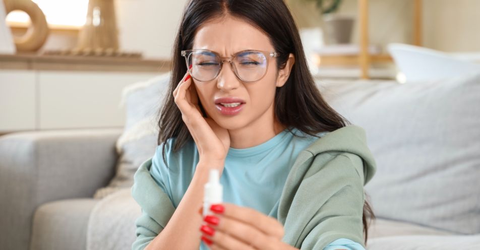 Woman holding ear drops and touching her ear, representing tinnitus and hearing changes